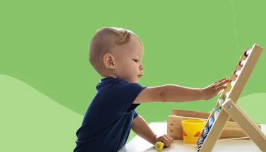 Un bébé joue à Montessori avec un chevalet en bois sur fond vert.