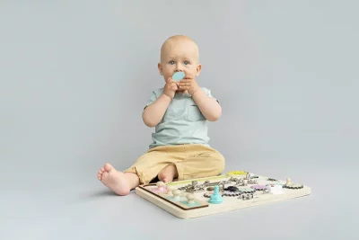 Bebe de 12 mois dans un fond studio jouant avec un Busy Board Montessori