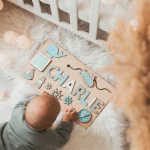 Ein Baby spielt mit einem personalisierten Puzzle mit Vornamen - aus Holz in einer Wiege.