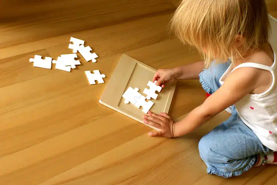 Ein dreijähriges Montessori-Kind spielt mit Puzzleteilen auf einem Holzboden.
