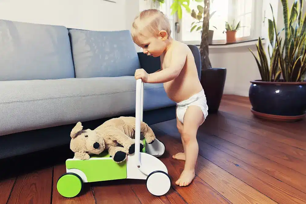 Un bébé joue avec un ours en peluche sur un char de marche.