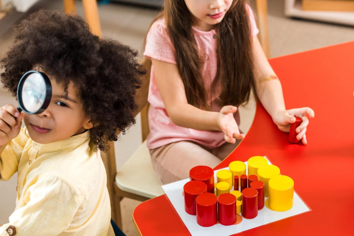 Un groupe d'enfants timides explorant à la loupe dans une salle de classe à l'aide de jeux Montessori.