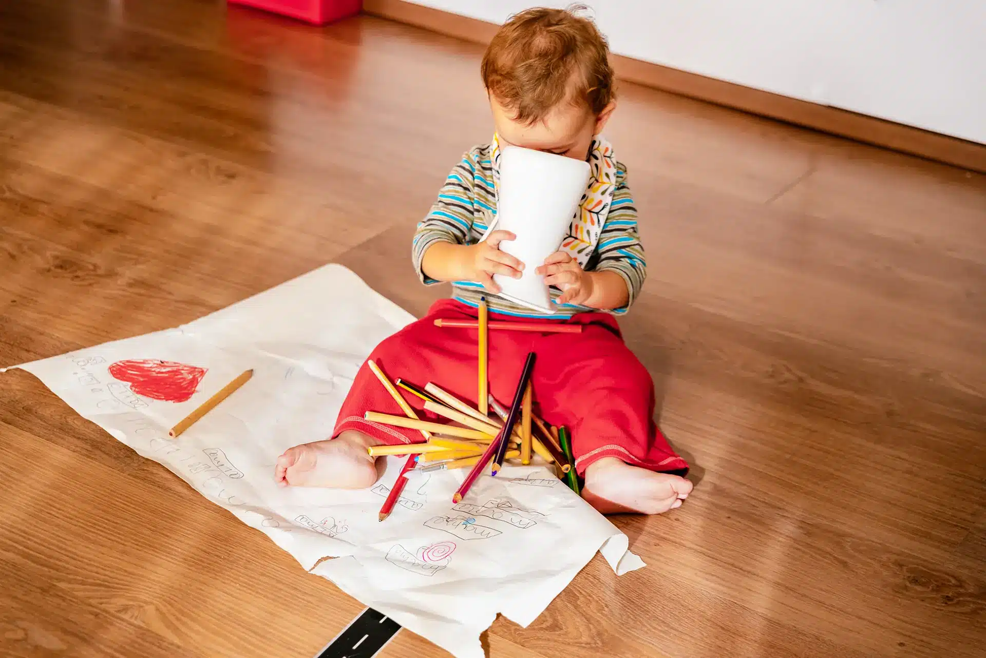 Ein einjähriges Baby spielt mit Stiften auf einem Holzfußboden.