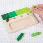 Eine Person hält ein Spiel mit Holzfiguren - Farben zusammensetzen, ein Holzspielzeug mit grüner Farbe darauf.