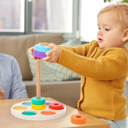 A baby plays with a colorful toy on a table called a “Stringing Circles Game.”
