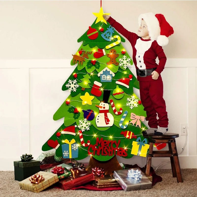 A child dressed as Santa Claus stands next to a Felt Christmas Tree - 26 Decorative Pieces + Lighted Garland - 95cm, decorated with felt.