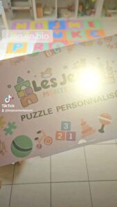 Une affiche pour « Les Jeux Montessori » présentant un puzzle personnalisé est affichée, avec des tapis de jeu colorés visibles en arrière-plan.