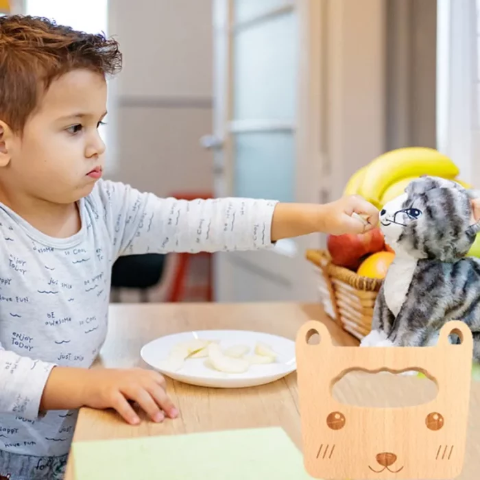 A young boy feeds a wooden cat toy.