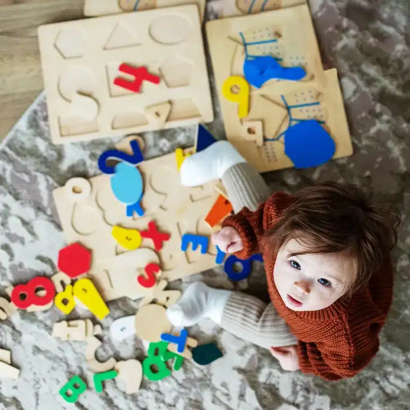A baby sitting on a carpet with wooden puzzles.