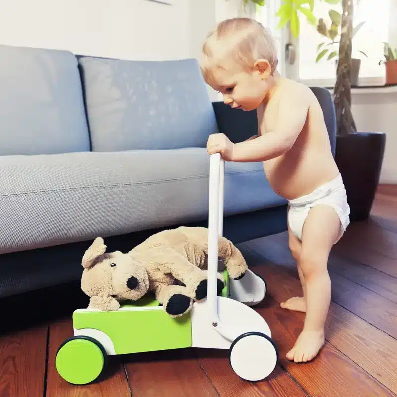 Un bébé joue avec un ours en peluche sur un jouet en bois.