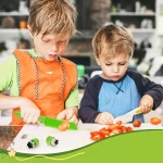 Zwei Jungen schneiden mit dem Kindermesser - Set aus 8 Küchenwerkzeugen Gemüse auf einem Schneidebrett.