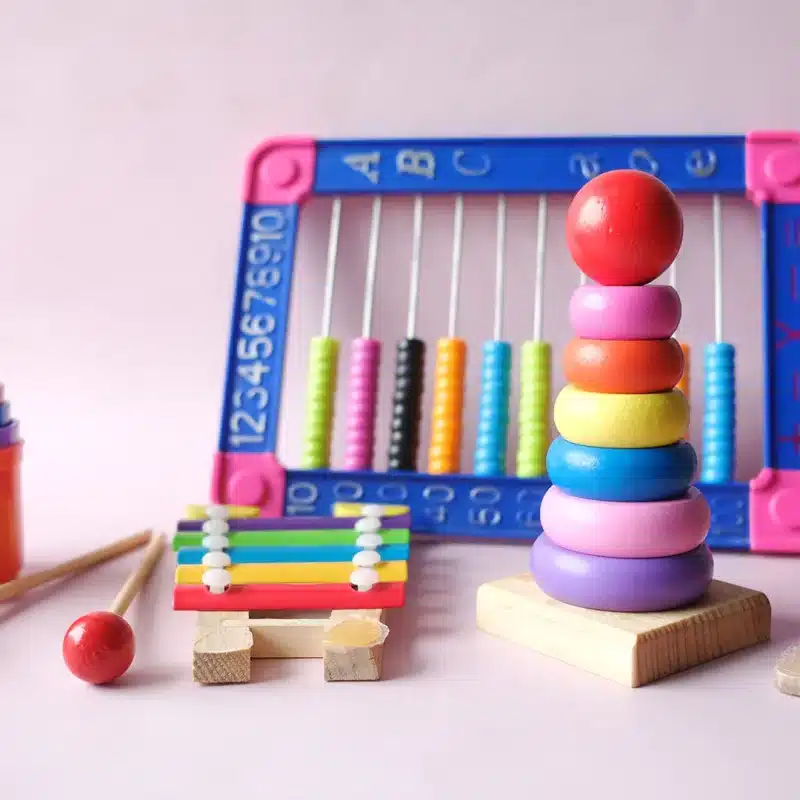 Une pile de jouets en bois et un boulier en bois sur fond rose.