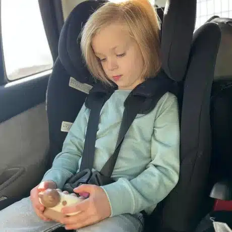Une petite fille dans un siège auto tenant le QuickPush - Jouet de réflexe et vitesse dès 3 ans, démontrant des réflexes vifs et de la rapidité.