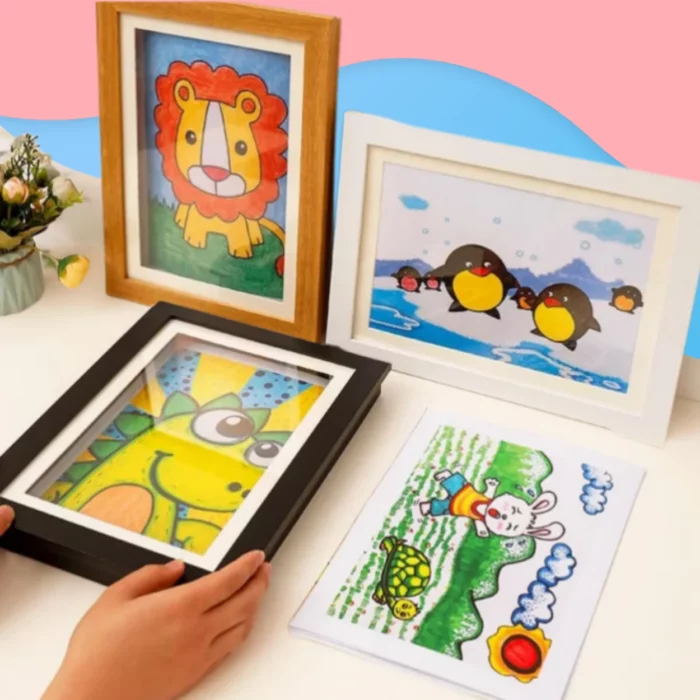 Quatre dessins d'animaux colorés en taille A4 (lion, pingouins, girafe, lapin avec tortue) exposés sur une table blanche avec un fond rose et bleu-parfait avec le Cadre pour dessins d'enfant pour stocker et exposer 150 œuvres.