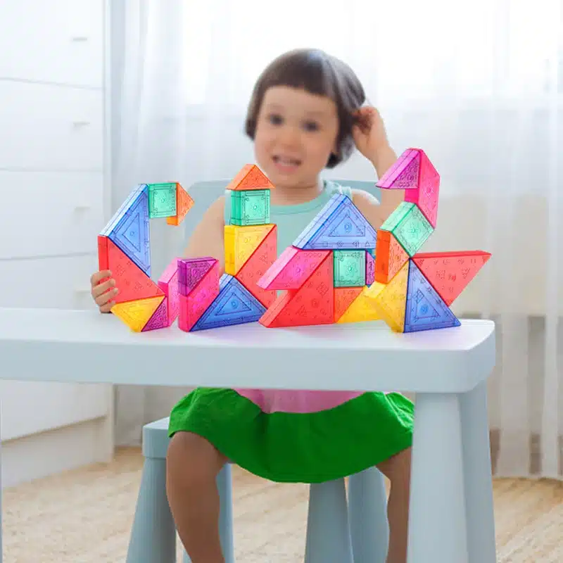 Une petite fille est assise à une table avec un Tangram Magnétique.