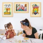 Une femme et une jeune fille se livrant à des activités de peinture autour d’une table avec des œuvres d’art colorées dans un Cadre pour dessins d’enfants - stockez et exposez 150 dessins - taille A4 sur le mur derrière elles.