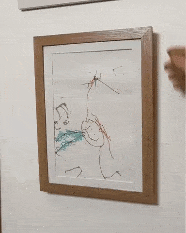 Une personne fait pivoter un tableau encadré, ou cadre dessin, sur le mur, révélant un compartiment caché derrière lui avec plusieurs clés accrochées à des crochets.