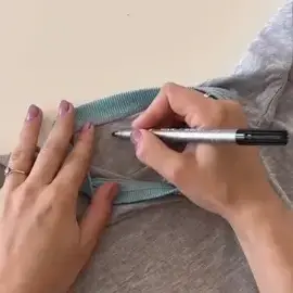 Une personne utilise un tampon pour tracer le contour d’un objet rond bleu sarcelle sur un tissu gris.