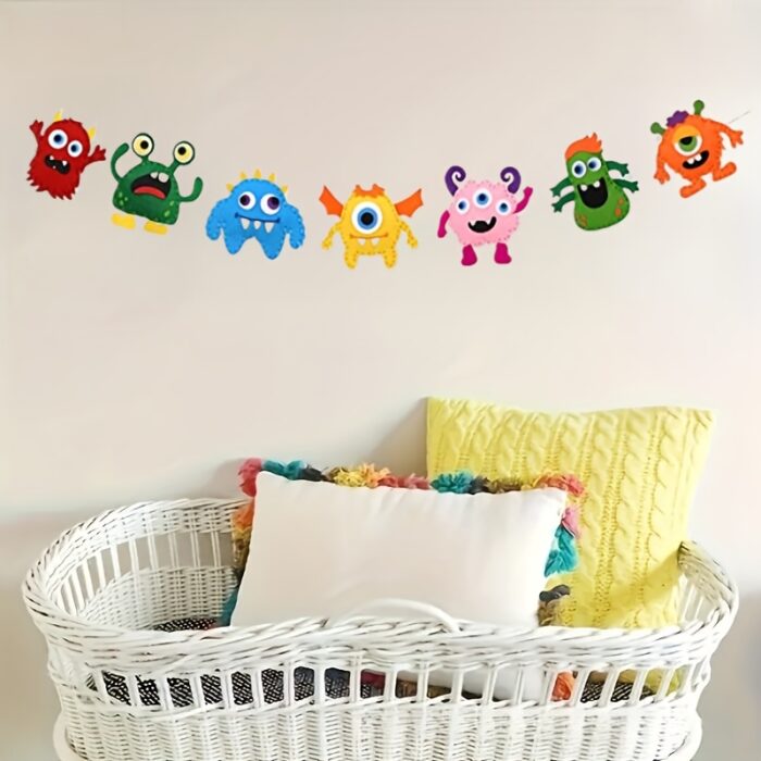 Un berceau en osier blanc avec des coussins colorés se trouve sous un mur orné d'une guirlande de découpes de monstres de dessins animés, idéal pour présenter les créations du Kit de Couture Enfants - Porte-clés à Faire Soi-Même Sans se piquer le doigt.