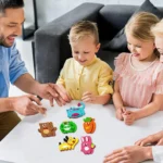 Trois enfants et un adulte sont assis à une table et interagissent avec des jouets colorés en forme d'animaux. Le décor semble être un environnement intérieur décontracté.