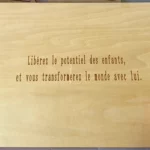 Plaque en bois avec texte gravé en français : " Libérez le potentiel des enfants, et vous transformerez le monde avec lui.