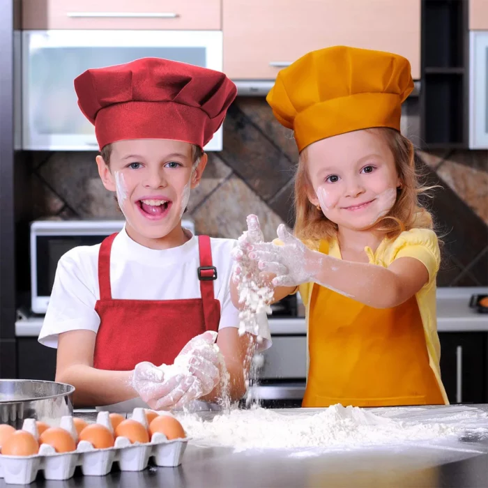 Deux enfants dans une cuisine portant des toques et des tabliers de chef jouent avec de la farine sur un comptoir près d'un carton d'œufs.