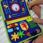 Un enfant s'engage avec un tableau d'activités coloré, un kit sensoriel ravissant comprenant une horloge, des engrenages, des fermetures à glissière et divers éléments tactiles vibrants pour un apprentissage et un jeu immersifs.