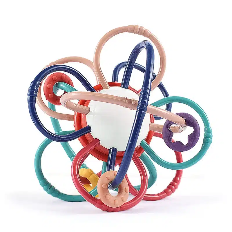 Le Hochet multi fonction- Montessori est un hochet pour bébé multicolore avec des boucles entrelacées autour d'une sphère blanche centrale.