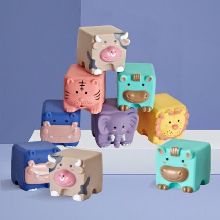 Le Cube d’éveil bébé en silicone – Animaux présente des animaux jouets colorés en forme de cube comme un tigre, une vache, un éléphant, un lion et un hippopotame disposés de manière ludique sur un fond bleu et violet.