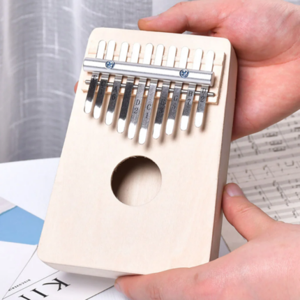 Une personne tient un kalimba en bois avec des dents en métal, étiquetées avec des notes de musique, au-dessus d'une table.