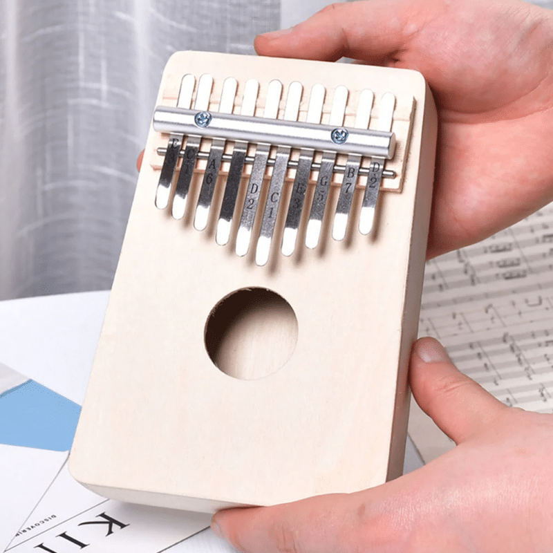 Une personne tient un kalimba en bois avec des dents en métal, étiquetées avec des notes de musique, au-dessus d'une table.