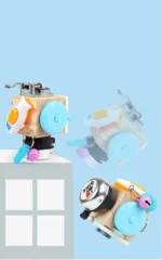 Deux robots jouets ressemblant au « Mini Busy Board Musical », avec des pièces colorées assorties comme des roues et des cloches, sont disposés sur un fond bleu clair. L'un d'eux apparaît posé sur le bord d'une plate-forme, prêt à se lancer dans une action musicale.