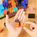 Quelqu'un dispose de petits blocs de mines à motifs de lave de « Mine Blocks - L'univers virtuel dans la vie réelle » sur une table en bois avec d'autres pièces colorées, fusionnant des thèmes virtuels avec la créativité de la vie réelle.